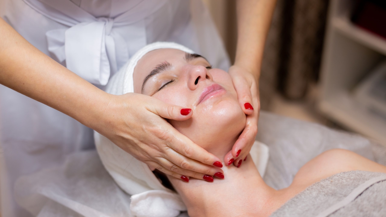 A young beautiful girl lies on the beautician's table and receives procedures, a light facial massage. Woman takes care of herself, enjoys massage